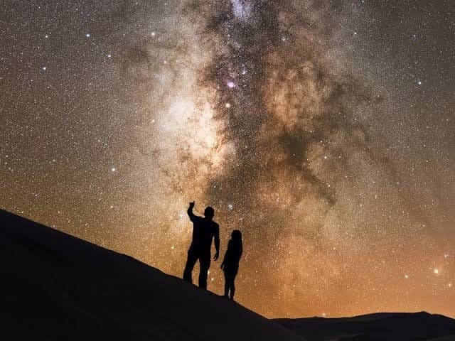 Silhouettes pointing at Milky Way